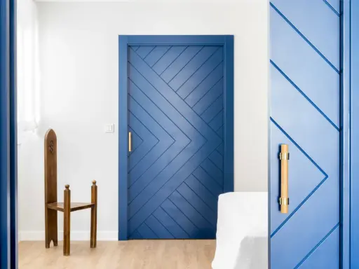 Puertas azules interiores con diseño geométrico y tiradores de madera. Una silla de madera antigua destaca junto a una de las puertas.
