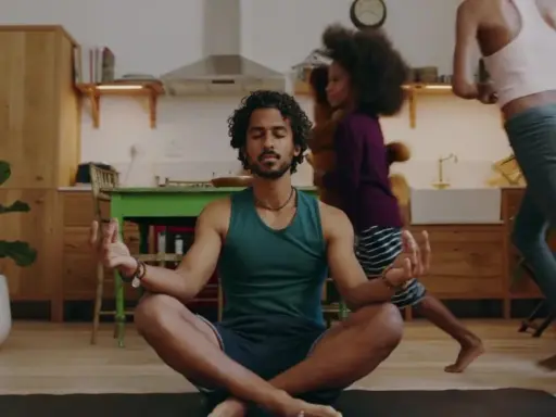 Man i lugn meditation i köket medan barn springer förbi. En lugn stund för 5 minute meditation mitt i vardagskaoset.