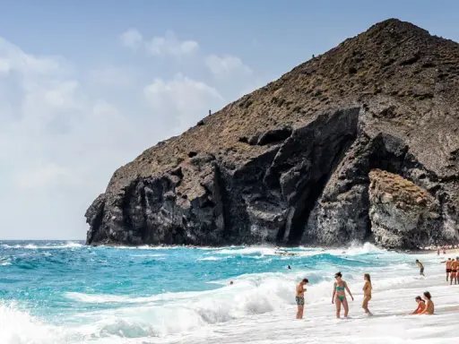 Sonniger Almería Urlaub: Menschen genießen den Strand und das Meer vor einer imposanten Felsformation.