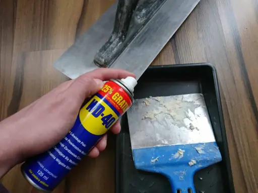 Spray WD-40 do czyszczenia zaschniętego betonu z narzędzi. Na zdjęciu puszka WD-40 i kielnia.