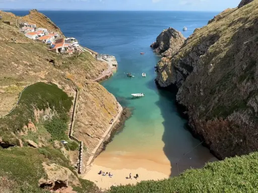 Idyllische Bucht mit weißem Sandstrand und türkisfarbenem Wasser auf den Berlengas Inseln. Kleine Boote ankern, Häuser schmiegen sich an die Felsen.