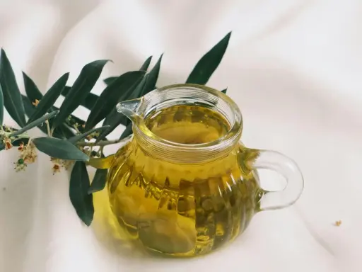 Aceite de oliva dorado en jarra de cristal, junto a rama de olivo. ¿Cuál es el aceite de oliva más suave?