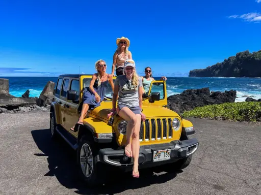 Fyra glada kvinnor på en gul jeep vid havet. Drömmen om att flytta till Hawaii känns nära!