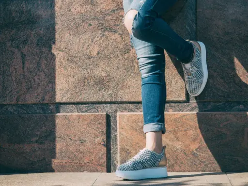 Kobieta w podartych jeansach i modnych sneakersach. Pokazano, jak podwinąć spodnie, by uzyskać stylowy efekt.