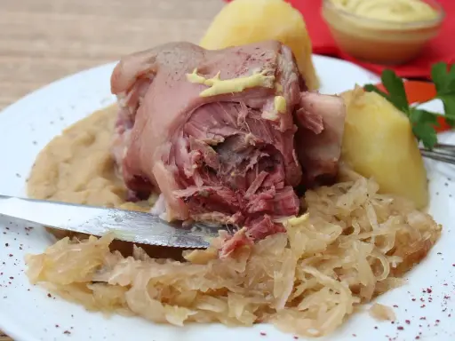 Un plat copieux de spécialités culinaires alsaciennes : jarret de porc, purée de pommes de terre et choucroute, garni de moutarde.
