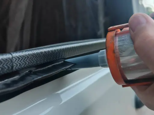 Application de mastic Sika 265 sur un joint de fenêtre de véhicule pour une étanchéité parfaite.