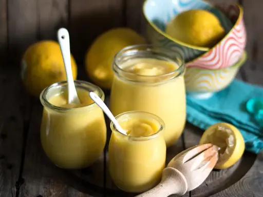 Drei Gläser mit cremigem Lemon Curd, Löffel und frische Zitronen. Perfekt für ein einfaches Lemon Curd Rezept.