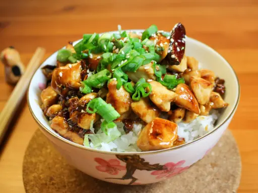 Schüssel mit Reis, Hähnchen und Frühlingszwiebeln, garniert mit Sesam. Ein köstliches Kung Pao Gericht, bereit zum Genießen.