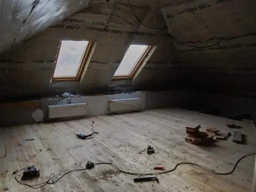 Chantier sous les combles : pose du frein vapeur, deux fenêtres de toit, radiateurs et outils sur le plancher en bois.
