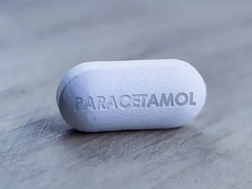 Biała tabletka z napisem "PARACETAMOL" na szarym tle. Dylemat: apap czy paracetamol?