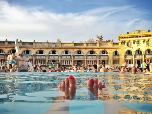 Fötter sticker upp ur vattnet i ett soligt budapest spa. Människor badar och njuter av den vackra arkitekturen.