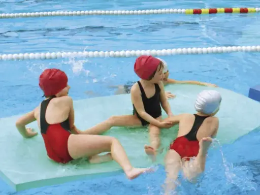 Niños divirtiéndose con juegos en la piscina, sentados en flotadores y chapoteando.
