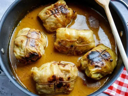 Fünf Kohlrouladen im Topf, bereit für ein köstliches Kohlrouladen Rezept. Eine Holzspatel liegt daneben.