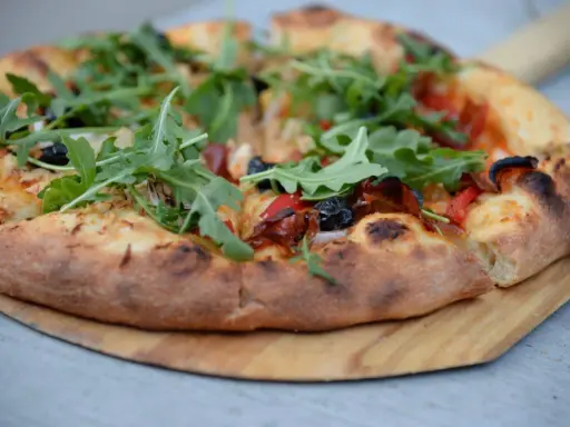 Pyszne ciasto na pizzę z rukolą, oliwkami i papryką, podane na drewnianej desce.