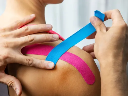 Aplikacja kinesiotapingu. Różowe i niebieskie plastry na ramieniu. Kinesiotaping co oznaczają kolory?