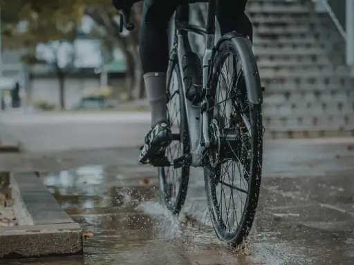 Rowerzysta w deszczu, koła rozpryskują wodę. Montaż błotnika rowerowego zapewnia suchą jazdę.