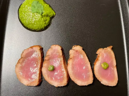Cuatro lonchas de tataki de salmón con un toque de verde y una guarnición vibrante.