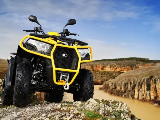 Un quad amarillo listo para conducir por terrenos escarpados junto a un río.
