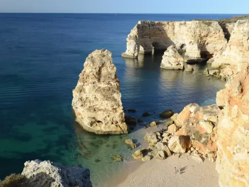 Felsformationen und türkisfarbenes Wasser an der Praia da Marinha, Algarve. Ein einsamer Felsen ragt aus dem Meer.