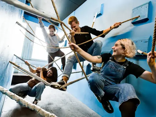 Fyra glada vänner klättrar i rep och njuter av utomhus aktiviteter. De skrattar och håller i repen, en del sitter, andra står.