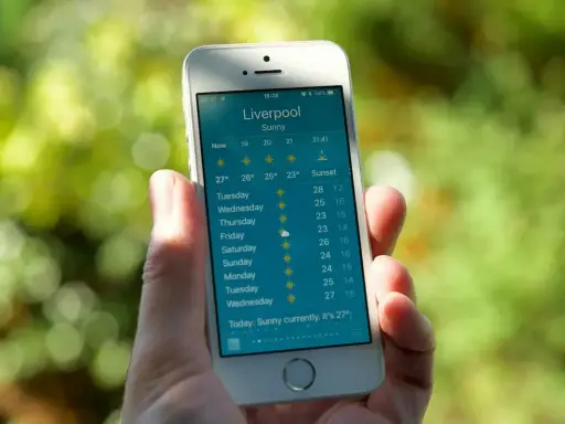 Dłoń trzyma smartfon z wyświetloną prognozą pogody dla Liverpoolu. To najlepsza aplikacja pogodowa, pokazująca słoneczną pogodę i temperatury na najbliższe dni.