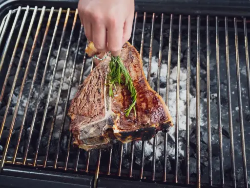 Ein saftiger florentiner steak wird mit Rosmarin auf dem Grill verfeinert.