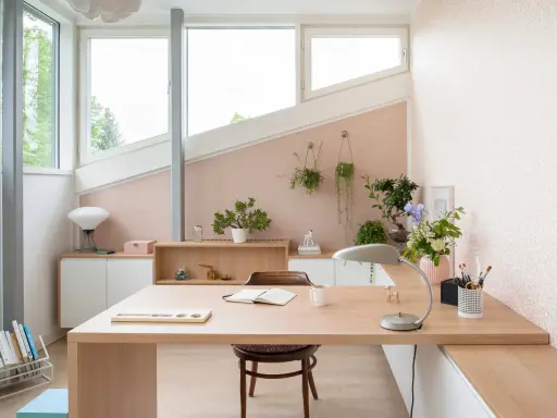 Une petite chambre avec bureau, lumineuse et décorée de plantes. Le bureau en bois clair est prêt pour le travail ou la lecture.