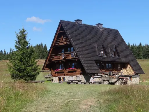 Drewniana bacówka na Krawcowym Wierchu, otoczona zielenią i lasem. Obok stoi stary traktor.