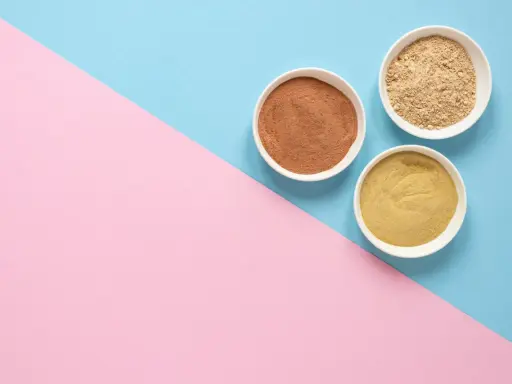 Tres cuencos blancos con polvos de diferentes tonos, como masilla para pared interior, sobre un fondo dividido en rosa y azul.