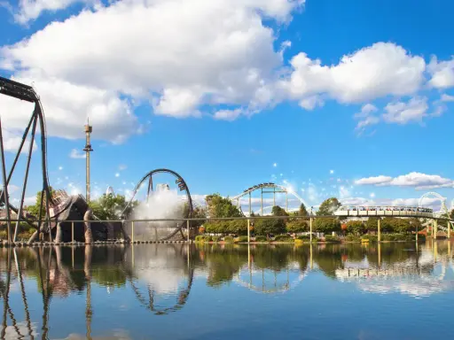 Aussicht auf Achterbahnen und einen Freizeitpark mit Spiegelung im Wasser.