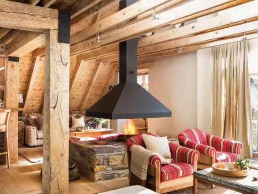 Chimenea central de diseño moderno, uno de los tipos de chimeneas que aporta calidez a este salón rústico con vigas de madera.