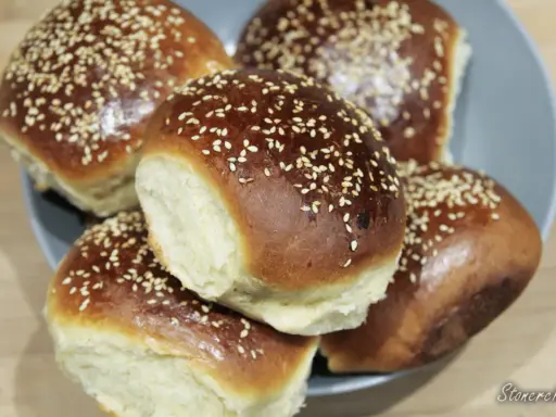Pięć puszystych bułek do burgerów, posypanych sezamem, ułożonych na talerzu. Idealne na domowe burgery.