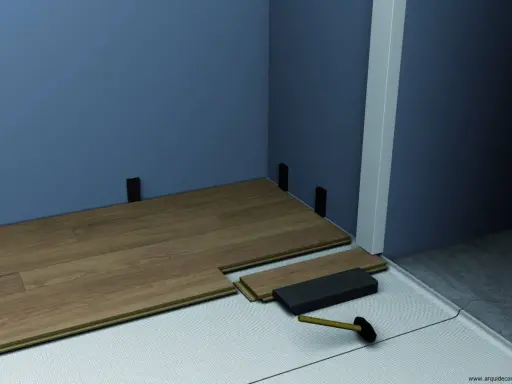 Instalación de suelo laminado. Se ven piezas de madera, un mazo y soportes para el rodapié que es la pieza final.