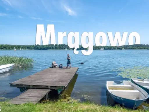 Mrągowo atrakcje: spokojny dzień nad jeziorem, dzieci łowią ryby z pomostu, żaglówki na horyzoncie.