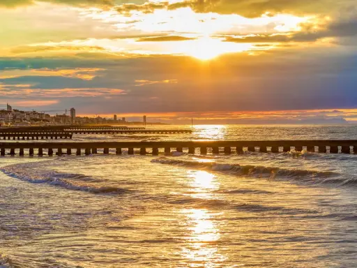 Tramonto dorato sul mare veneto, con moli che si estendono nell'acqua e una città all'orizzonte.