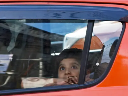 Niño mira por la ventana del coche, apoyado en el cristal, sin silla en el coche. Reflejos en el vidrio.