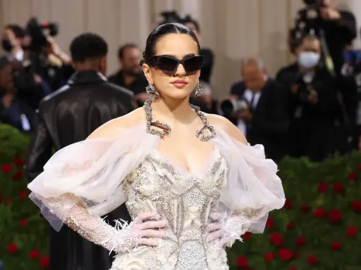 Rosalía deslumbrante en la Met Gala, con un vestido blanco adornado y gafas de sol vanguardistas.
