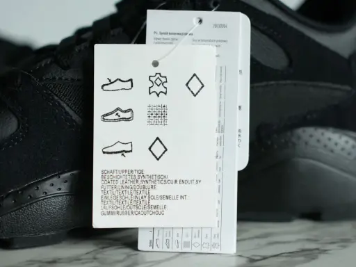 Czarna cholewka w adidasach, wykonana z połączenia skóry i materiałów syntetycznych, z widoczną metką z symbolami pielęgnacji.