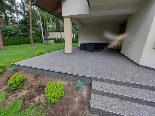 Nowoczesna nawierzchnia mineralno żywiczna tarasu i schodów, otoczona zielenią.