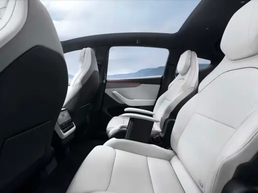 Interni bianchi e neri del Tesla Model Y, con sedili in pelle, tetto panoramico e vista sulle montagne.
