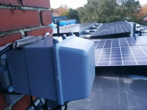 System podgrzewania paneli fotowoltaicznych zamontowany na dachu, obok ceglanej ściany.