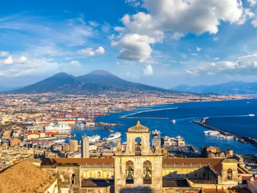 Vista di Napoli con il Vesuvio sullo sfondo, un porto vivace e un campanile antico. Un gioiello tra i siti UNESCO Campania.