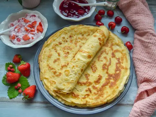 Omas Pfannkuchen-Rezept: goldbraune Pfannkuchen auf einem Teller, dazu Erdbeerquark, Kirschmarmelade und frische Erdbeeren.