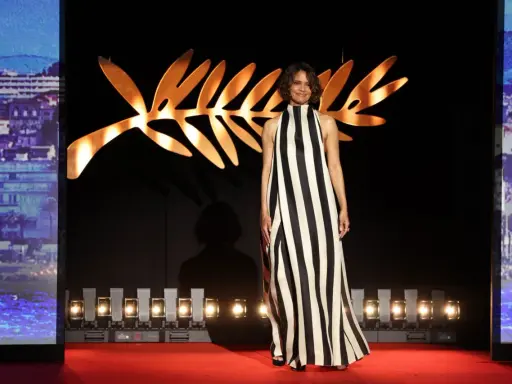 A woman in a striking black and white striped gown poses on the Cannes Film Festival red carpet, bathed in the glow of the iconic Palme d'Or backdrop.
