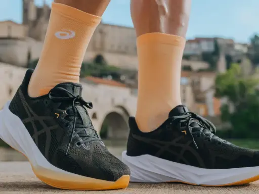 Biegacz w pomarańczowych skarpetkach z logo Asics i ciemnych butach tej firmy, gotowy do podboju miasta.