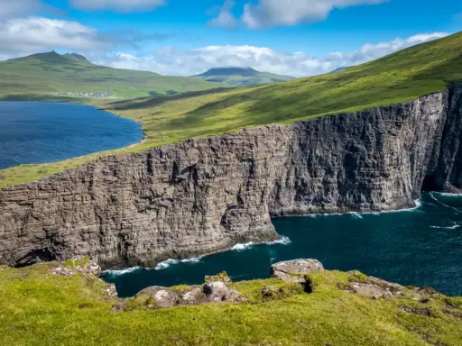 Scogliere imponenti e un lago blu intenso nelle Isole Faroe, dove gli abitanti vivono in armonia con la natura selvaggia.
