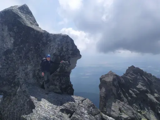 Wspinacz w kasku na skalistym szczycie, podziwiający widok. Tatry poza szlakiem, gdzie każdy krok to przygoda.