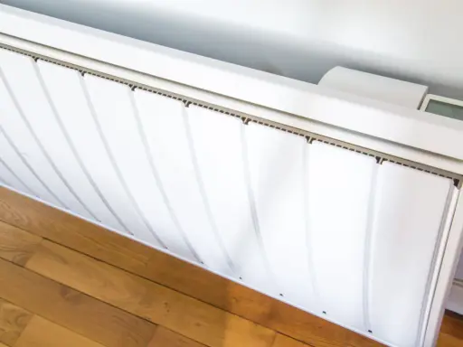 Radiateur électrique blanc installé sur un parquet. Un écran affiche la température. Guide pour comment installer un radiateur électrique.