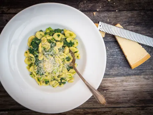 Orecchiette mit Cime di Rapa, frisch geriebenem Parmesan und einem Löffel auf einem Holztisch.
