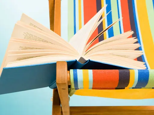 Un libro aperto, pieno di classici della letteratura, appoggiato su una sdraio a righe colorate.